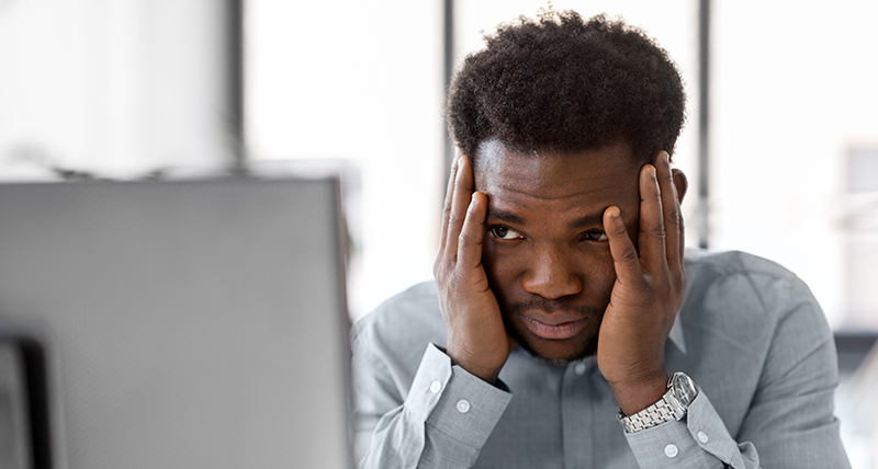 Man in grey shirt looking at computer screen with head in hands